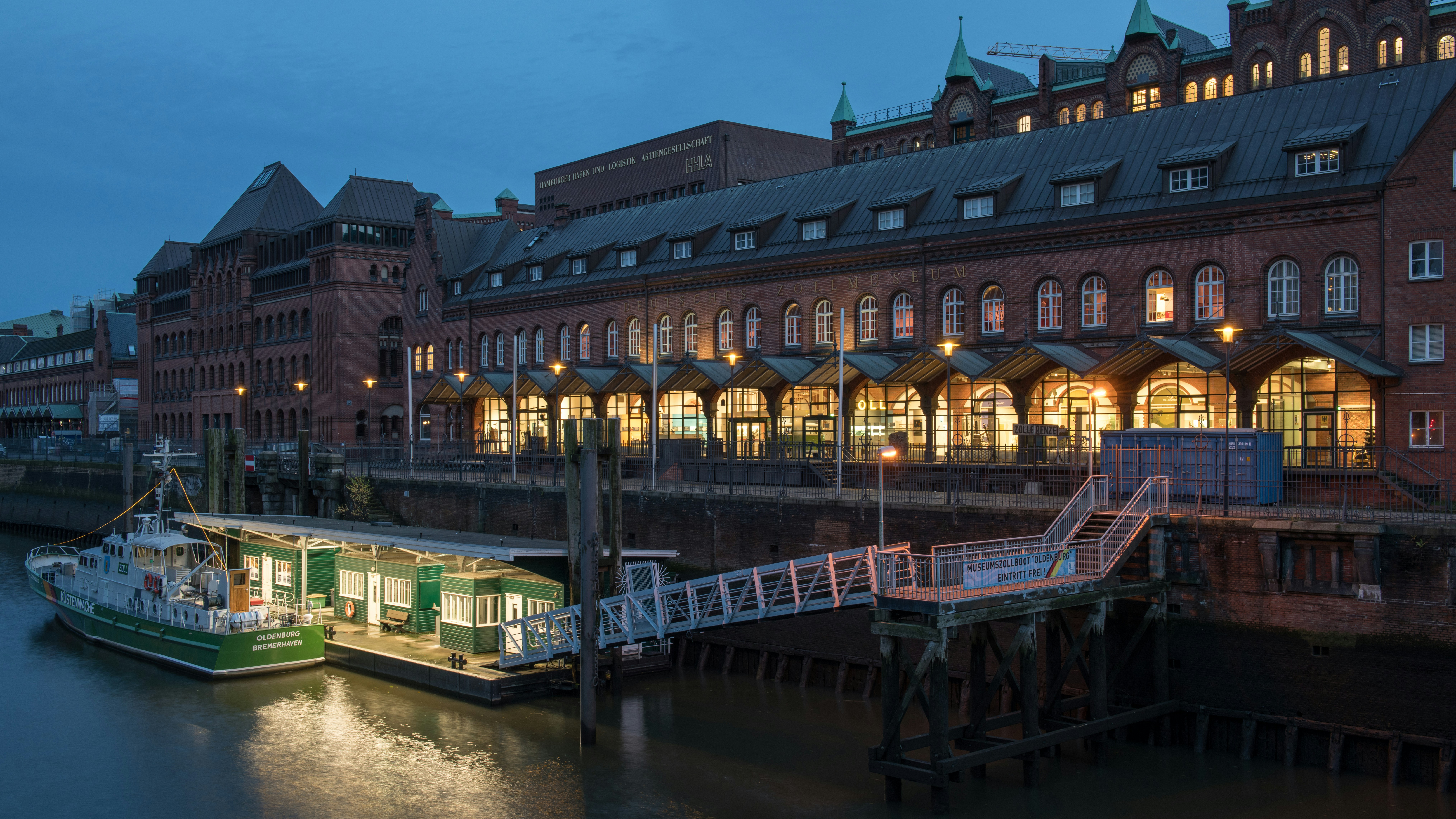 An illuminated building sits by the water at dusk